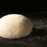 A smooth, round ball of dough resting on a dark, flour-dusted surface against a black background.