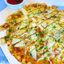 A close-up of a baked flatbread pizza cut into long strips on a wooden serving board, topped with melted cheese, parmesan cheese slices, and chopped green herbs, with a small bowl of red sauce for dipping.